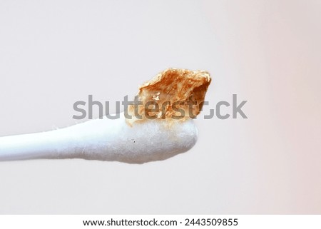 Ear wax plug isolated on white background. Removed giant ear wax plug on cotton swab closeup. Wax, which is also called cerumen on swab, macro shot. Cotton swab and ear hygiene. Remove earwax buildup Royalty-Free Stock Photo #2443509855