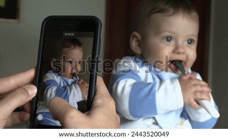 Parent taking photo of baby. Mother filming infant child with cellphone