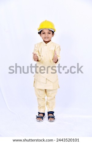 Indian little boy wearing yellow hard hat and showing thumps up on white background