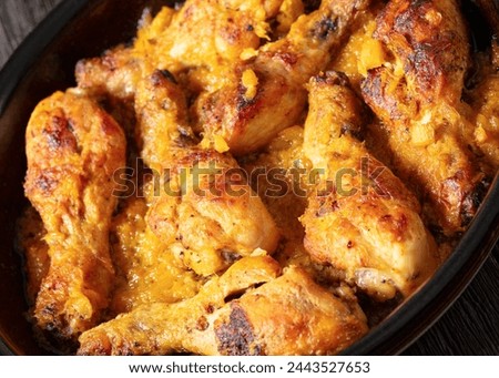 close-up of chicken drumsticks baked in crushed pineapple sauce in black dish on dark rustic wooden table, dutch angle view Royalty-Free Stock Photo #2443527653