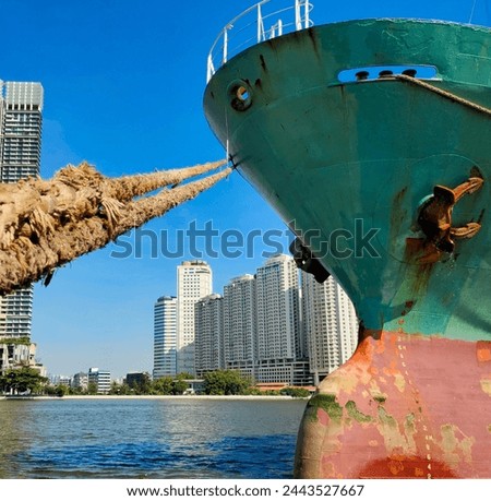 Anchor on large cargo ship's anchor being pulled, Green and red ship, While docked at the pier by large ropes on the river, in the background is a view of the city's buildings and transport concept
