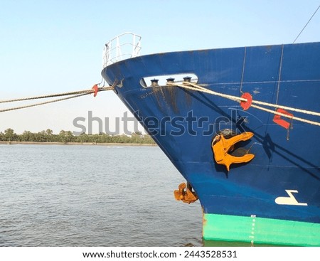 Anchor with large cargo ship, rusty anchor being pulled, Blue and Green ship, While docked at the pier by large ropes on the river, isoleted on river with blue sky background and transport concept