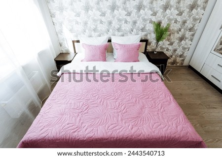 A pink bed with matching pillows in a bedroom, complete with a plant for added decor. The interior design includes purple accents and a sturdy bed frame