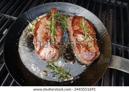 Zwei Steaks mit Rosmarinzweigen in der Pfanne auf dem Grill Royalty-Free Stock Photo #2443551691
