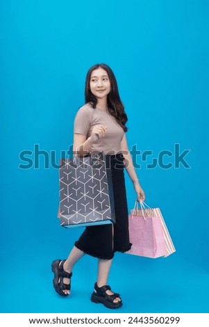 beautiful woman walking with a smile, her hands holding shopping bags isolated on blue background