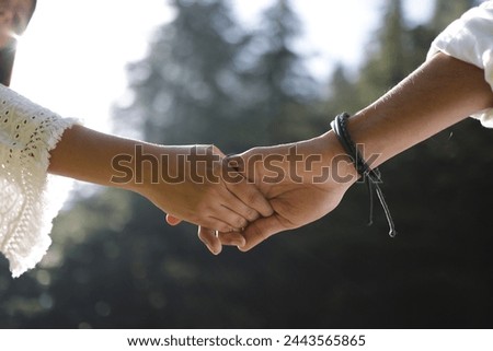 Two intertwined hands, fingers gently clasping, embodying affection, support, and unity—a symbol of profound connection and unwavering devotion. Royalty-Free Stock Photo #2443565865