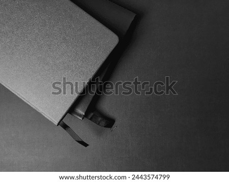 Two closed hardcover notebooks with a fabric bookmark. Minimalistic monochrome background
