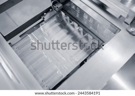 Operation of automatic machine plastic form for kit medical production. Closeup of roller blue toning, with sun lighting effect. Royalty-Free Stock Photo #2443584191