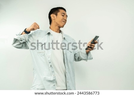 young man wearing a phone standing on a white background isolated with the proud phone and celebrating victory and success very excited while looking at the phone with a clenched fist.