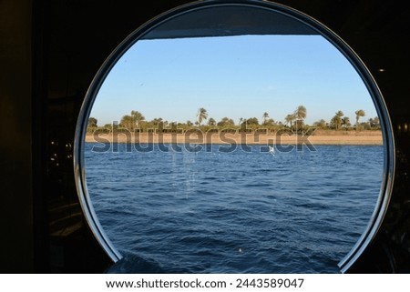 Daytime view of the river bank of the Nile through a cruise ship's port hole. Royalty-Free Stock Photo #2443589047