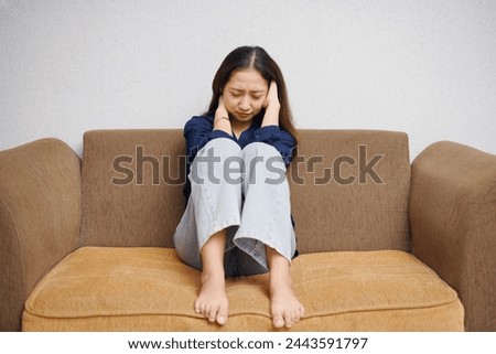 Asian woman sitting on the sofa with an expression that looks sad, anxious, full of fearv, feeling guilty Royalty-Free Stock Photo #2443591797