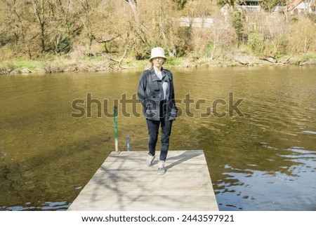 A woman stands on a small wooden pier near the Berunka River in early spring.