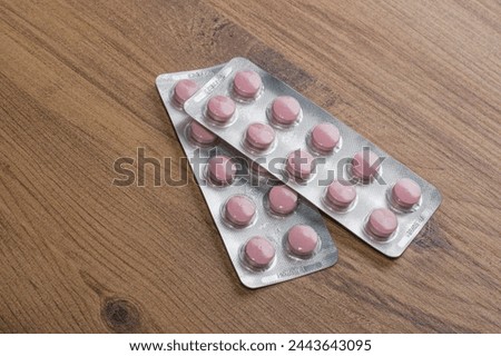 Pink pills in blistering aluminium packaging. Two medicine packs on a wooden table. Metaphor of modern medical instruments.