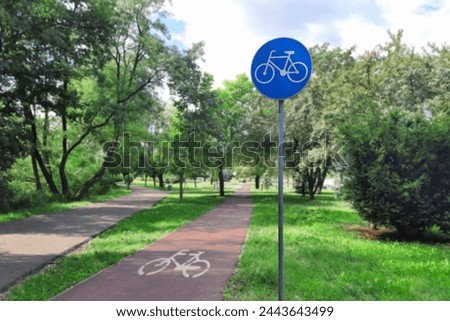 Bicycle path in a summer city park. Bike lane sign. Traffic sign white bicycle on blue circle and road markings on the asphalt. Concept of infrastructure development for ecological transport.