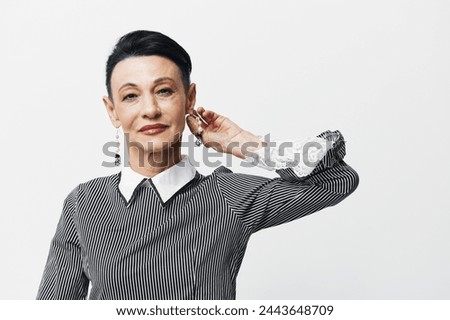 Elderly woman in black and white striped shirt posing with hand on ear for camera portrait shot