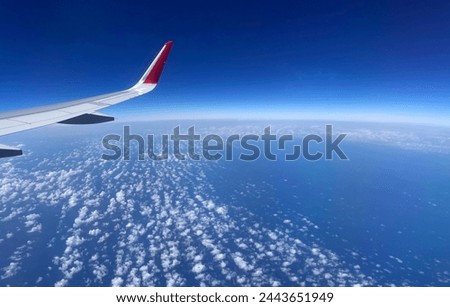 Exterior visual photo view from a planeof a wing through a window with the clouds seen from over the airplane with the earth curve of the planet we cansee like in space high altitude air