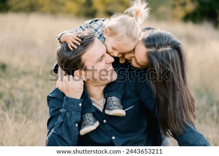 Mom with a little girl on the shoulders of dad kiss him, hugging from behind