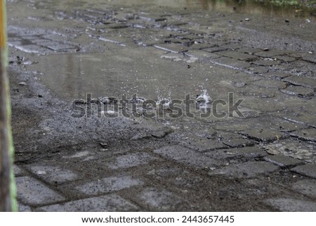 Photo of water splashing from a puddle on a paved road, the effect of raindrops