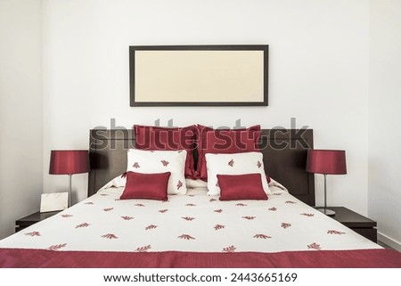 Bedroom headboard with double bed with upholstered bedspread and red satin cushions, dark wood furniture and twin lamps with bright red shades