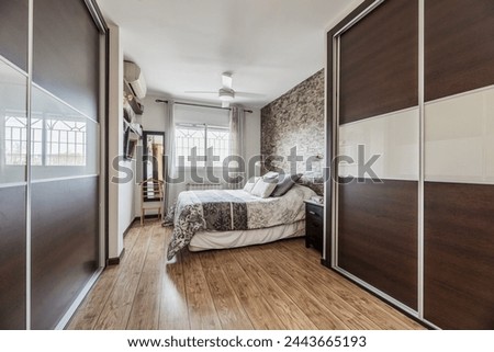 Large bed with several cushions in a gray bedroom with stone walls and imitation wood floors and two large built-in wardrobes with sliding doors