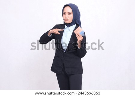 Mature Asian office woman wearing a hijab stands sullenly pointing and carrying a credit debit card for ease of making a bank savings book. adult Muslim blue shirt for finances, transactions and loans