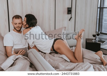 Intimate couple in bedroom, woman kissing man's forehead, cozy atmosphere, wine glasses on side table Royalty-Free Stock Photo #2443731883