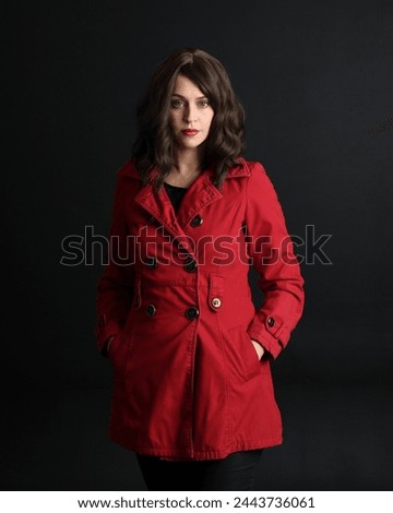 close up portrait of beautiful brunette woman model, wearing red trench coat.isolated on dark studio background with shadows.  hands in jacket pockets.