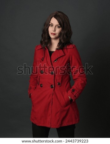 close up portrait of beautiful brunette woman model, wearing red trench coat jacket with gestural hands posing.isolated on dark studio background with shadows. 