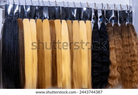 Diverse assortment of hair extensions, wigs, and accessories in various colors and textures for personal grooming and hairstyling at a beauty salon or industry market shop Royalty-Free Stock Photo #2443744387