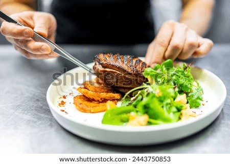 A meticulous chef artfully plates a grilled steak with roasted vegetables and fresh salad, showcasing culinary finesse. Royalty-Free Stock Photo #2443750853