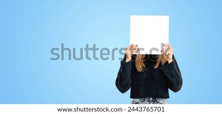 Young woman hiding face with mockup empty blank poster, wide format empty blue copy space background. Concept of emotion, plan, idea, ad, marketing or sale