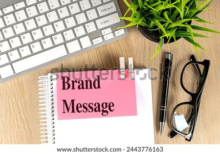 BRAND MESSAGE text pink sticky on a notebook with keyboard, pen and glasses . 