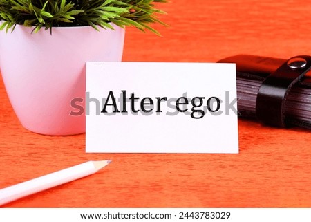 Alter ego It means the Second I written on a white business card next to a business card holder, pencil and plants in a white pot