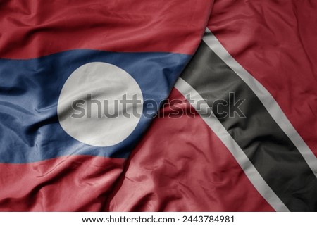 big waving national colorful flag of trinidad and tobago and national flag of laos. macro