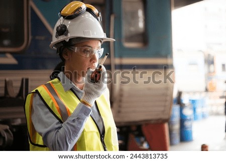 Portrait of railway technician worker in safety vest and helmet working and using a walkie talkie at train repair station Royalty-Free Stock Photo #2443813735