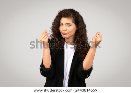 A confident young woman with curly hair snaps her fingers in a studio, wearing a black blazer over a white shirt Royalty-Free Stock Photo #2443814559