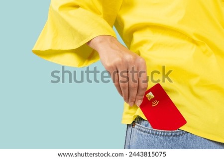 Close up cropped photo shot of female hand putting credit bank card in jeans pants denim front pocket isolated on blue studio background. Money finance currency concept