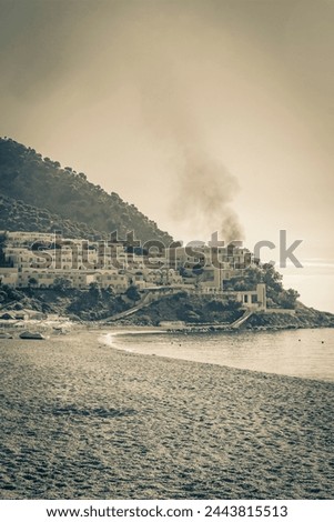Old black and white picture of a sunrise and smoke over luxury resorts and beaches sun loungers umbrellas under Oros Dikaios Dikeos mountain natural coastal landscapes Kos Island Greece with blue sky.