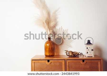 Bouquet of dried pampas grass flowers in a glass vase, mirrow, bronze figure of a beetle, wooden candle holder on brown drawers. Background with copy space, empty. Template, mockup for your design.