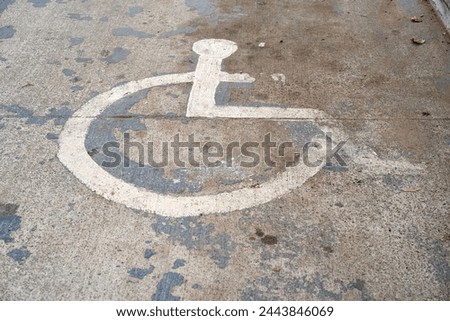 A close-up image capturing a faded and weathered handicap parking sign painted on the asphalt. The white iconic wheelchair symbol is partially worn, showcasing the effects of time and elements