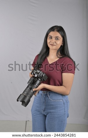 A young Hispanic woman photographer is smiling happily while standing and holding a camera. This image represents lifestyle, people, traveling, and photography.Stock image.