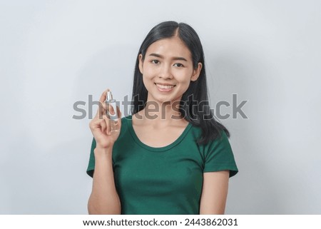 Beautiful young Asian woman in green t-shirt smells the aroma of perfume isolated on white background.