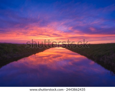 Nature. The river during a bright sunset. Bright sky with clouds during sunset. Landscape in the summertime. Reflections on the surface of the water.