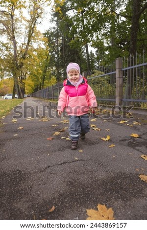 A smiling cute little girl in a pink jacket in fall. Vertical image. 