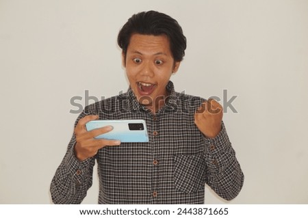 Excited young Asian man wearing black shirt playing game on smartphone isolated on white background 