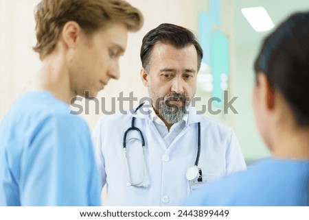 Group of medical staff standing and discussing together at the corridor in hospital. Senior doctor or medical professor explains and talks with students.