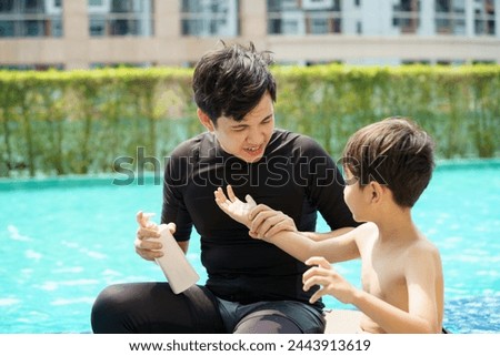 Father is applying a sun screen or sun block lotion on his son body before going to swimming in the swimming pool. Weekend vacation activities between father and son.