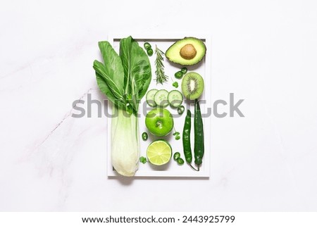 Artistic composition with fresh healthy vegetables, fruit and herbs on white marble background with white picture frame top view. Healthy vegan food concept.
