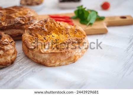 Baked pastry on white background with selective focus. Tomatoes and greens appear in blurred background. Appetising fast food lifestyle shot.
