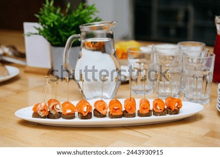 Elegant smoked salmon rolls with cream cheese served on bite-sized pumpernickel bread, beautifully presented on a serving plate for a gathering. Royalty-Free Stock Photo #2443930915